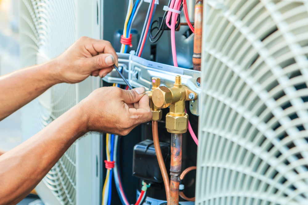 Close-up of a person’s hands using a tool to adjust wiring and components inside an air conditioning or HVAC unit.