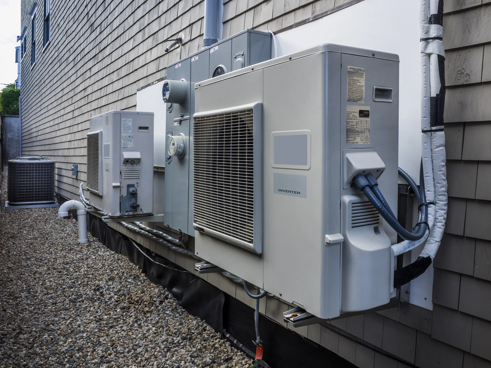 Several outdoor HVAC units mounted on the exterior wall of a building, with additional units visible in the background on a gravel surface.
